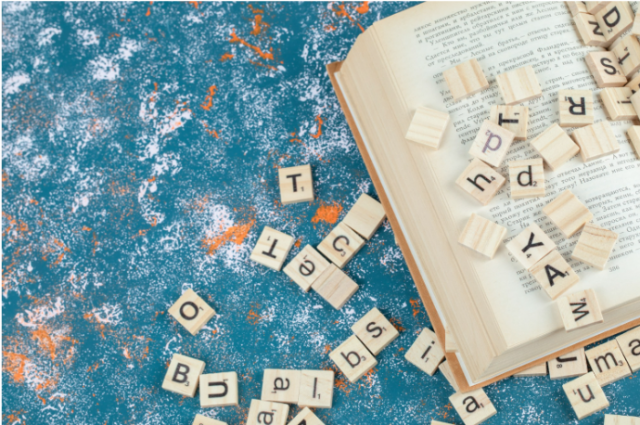 Open book with scattered wooden letter tiles on a textured blue surface, symbolizing reading challenges and dyslexia.