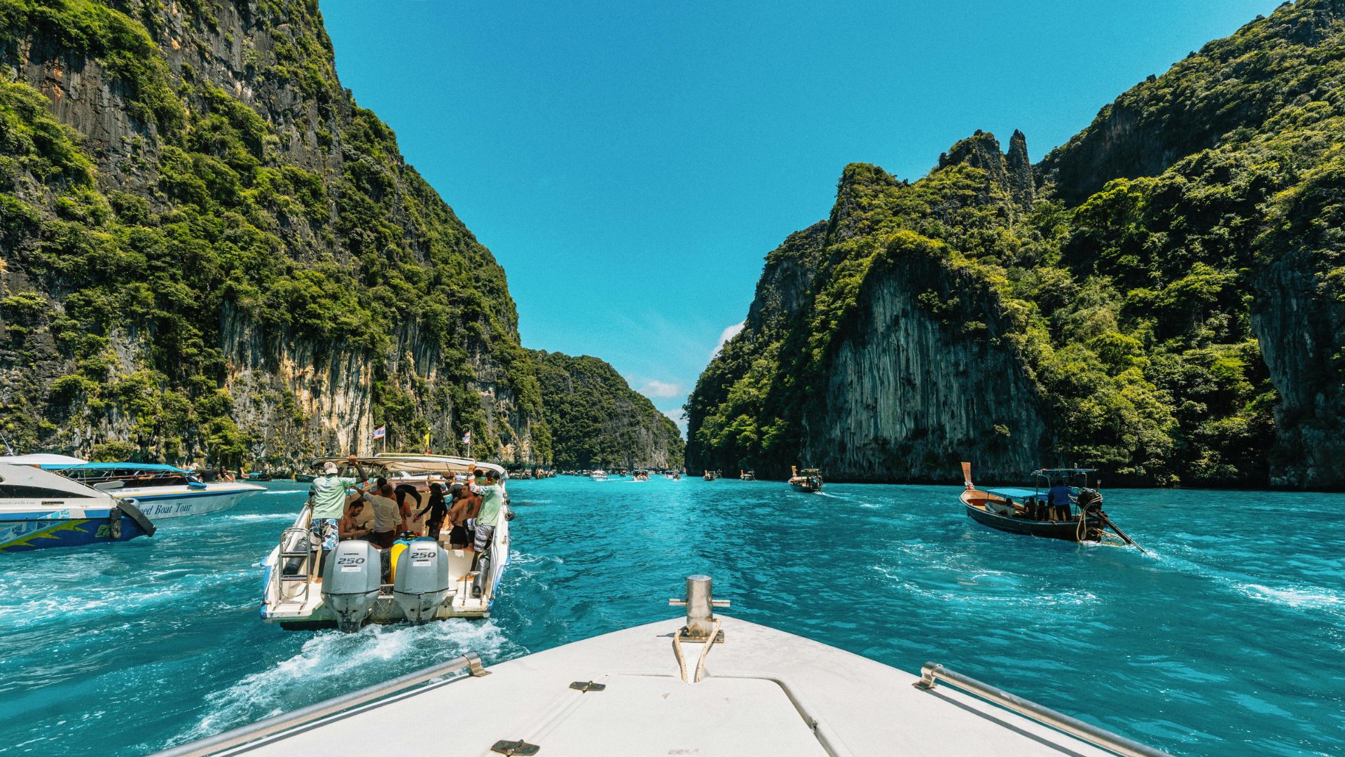 Traditional wooden long-tail boats resting on a beach in Thailand with limestone karst cliffs and blue water in the background