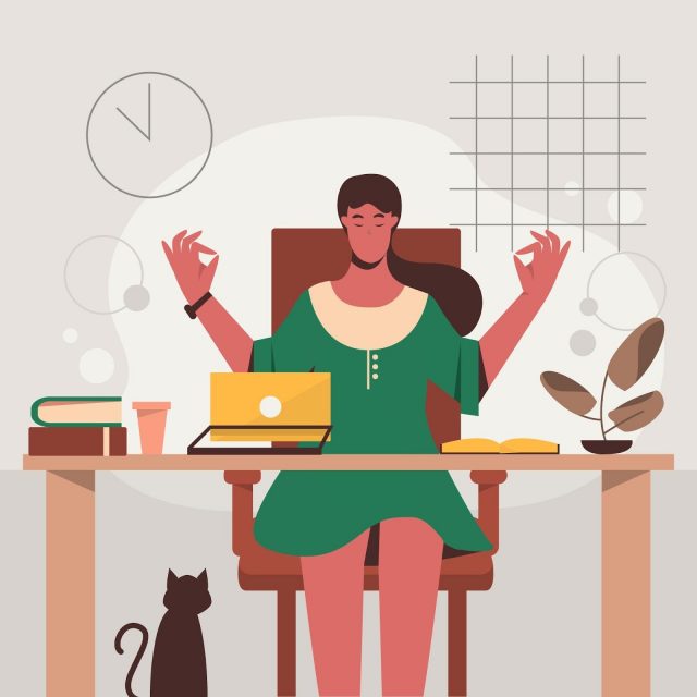 Woman meditating at office desk with laptop, books, plant, and cat nearby