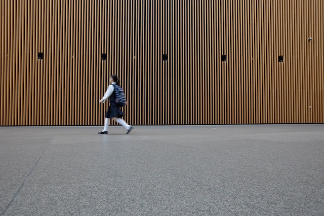 Girl walking to school by orange building christoph-theisinger-tIlnS6f9JBI-unsplash