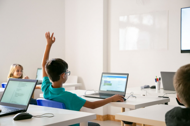A boy raises his hand in a classroom, eager to answer a question from the teacher.
