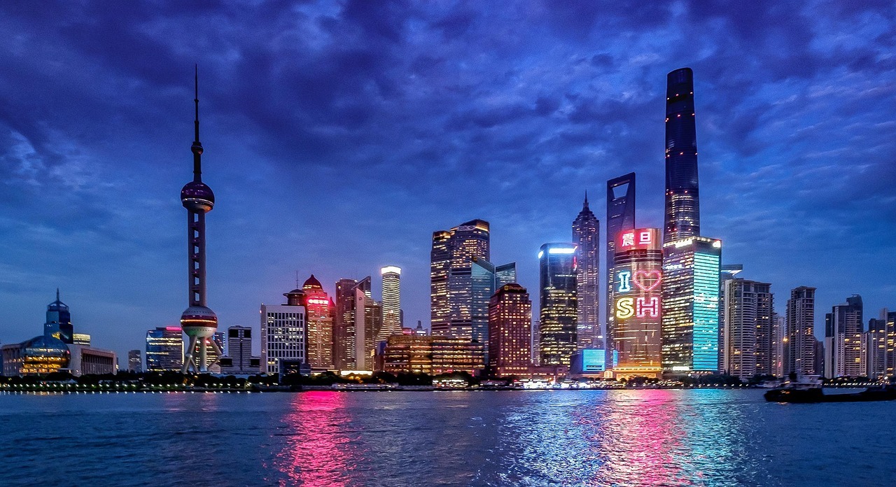 Modern skyscrapers along the waterfront of the Shanghai skyline featuring the Oriental Pearl Tower at dusk.