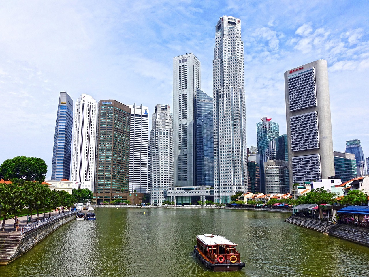 Modern skyscrapers along the waterfront of the Singapore skyline with green trees in the foreground.