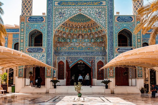 Detailed view of an ornate, blue-tiled Islamic building entrance featuring intricate geometric mosaics and calligraphy.