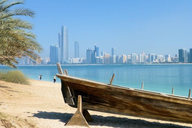 Traditional wooden dhow boat on a beach with a modern city skyline across the water, representing teaching English in the UAE.