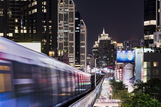 BTS Skytrain train moving past modern skyscrapers in Bangkok at night