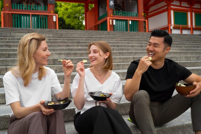 Three people sitting on outdoor steps eating street food together in Bangkok - Teaching in Bangkok