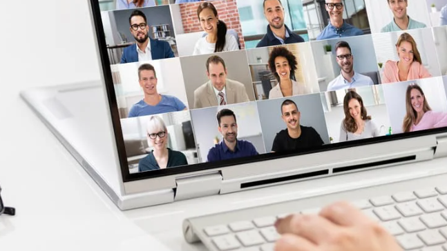 Person participating in a virtual meeting on a laptop, with multiple video call participants shown in a grid layout on screen