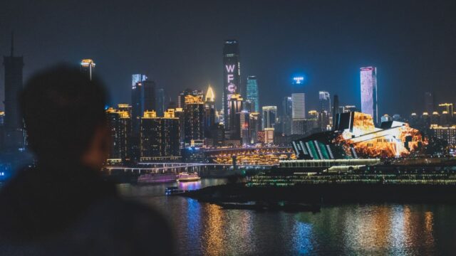 Silhouette of a person looking at the illuminated modern skyline of Shanghai across the Huangpu River at night.