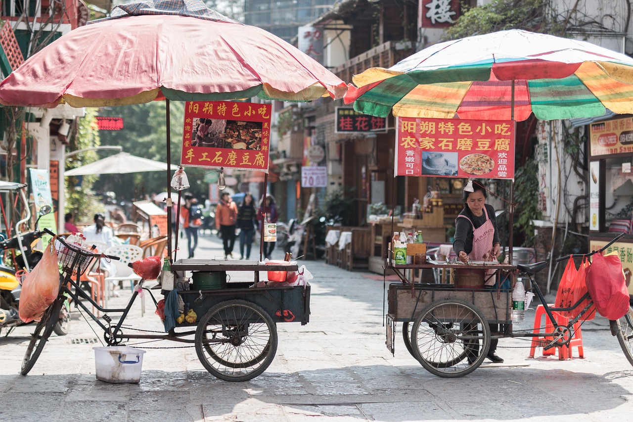 Two traditional Chinese street food carts with large colorful umbrellas parked on a narrow street in China.