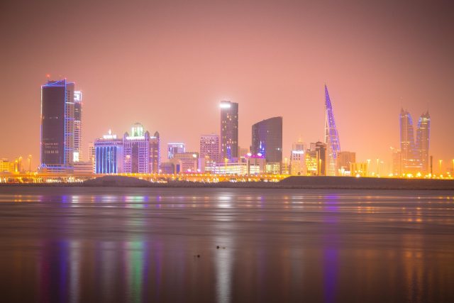 A vibrant city skyline illuminated at night, showcasing tall buildings and glowing lights against a dark sky.