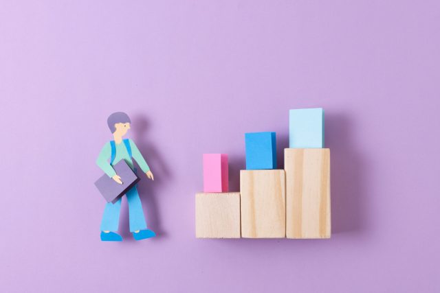 A paper cutout of a man on a wooden block next to a bar graph, representing statistical data visually.